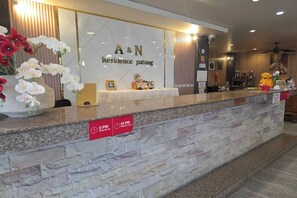 Un comptoir d’accueil avec un plan de travail en marbre, un panneau indiquant l’endroit où s’enregistrer et une plaque portant le nom de l’hôtel.