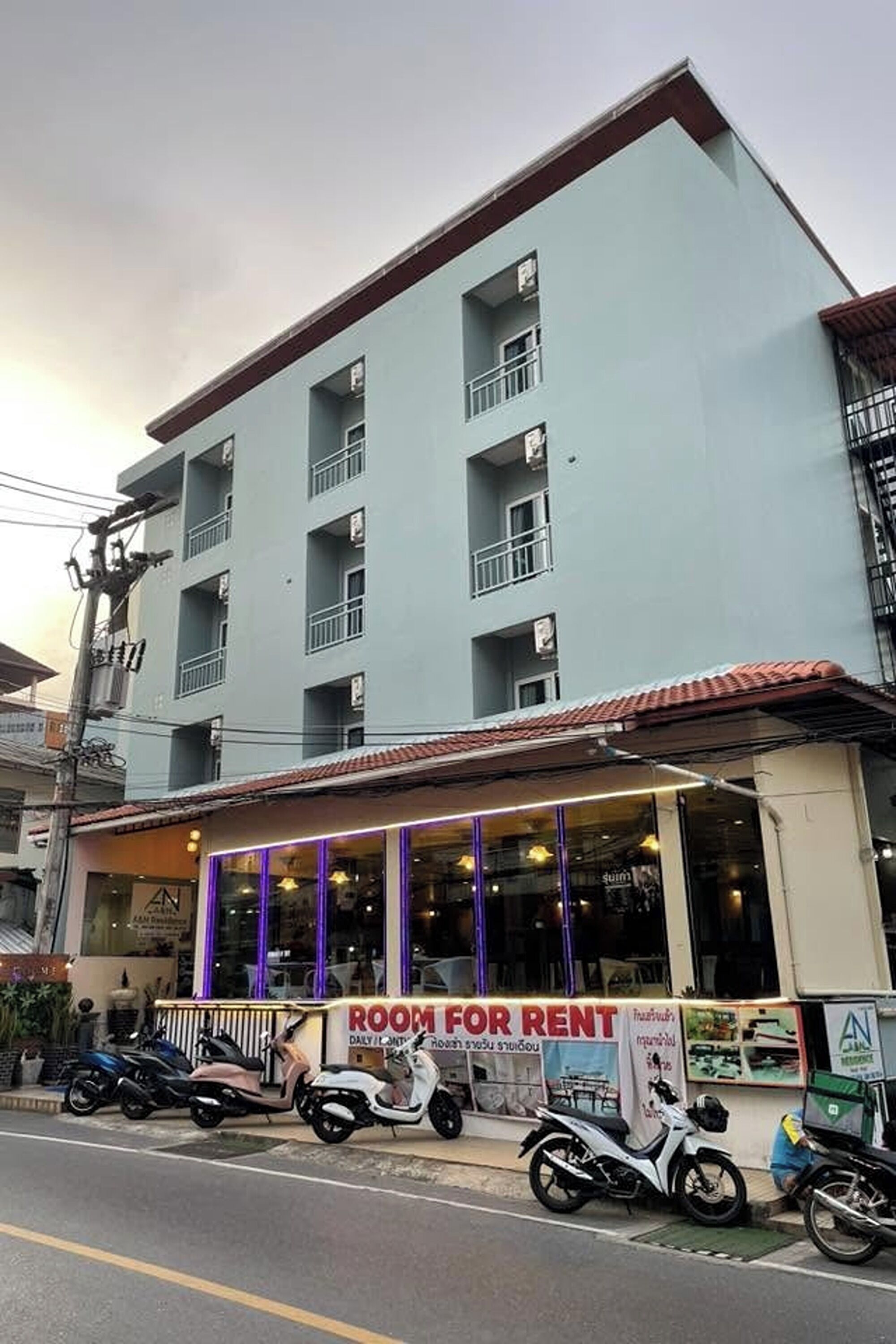 A multi-story building with a 'ROOM FOR RENT' sign, balconies, and parked scooters.