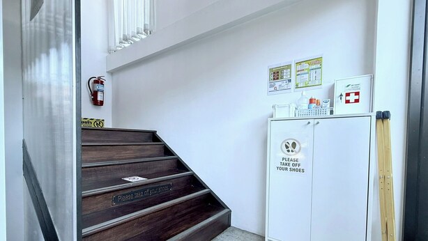 Una escalera con un cartel que indica quitarse los zapatos, un extintor y un mueble con un letrero solicitando quitarse los zapatos.