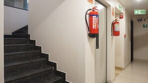 A hallway with a fire extinguisher mounted on the wall, a fire exit sign, and a staircase. - Executive Hotel Pearl Inn (Pune)