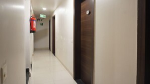A corridor with doors, a fire exit sign, and a fire extinguisher. - Executive Hotel Pearl Inn (Pune)