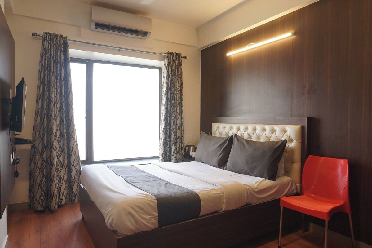 A hotel room with a bed, a red chair, a television, and a window with curtains.