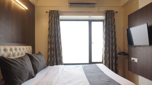 A hotel room with a large bed, a flat-screen TV mounted on the wall, and a window with curtains. - Executive Hotel Pearl Inn (Pune)