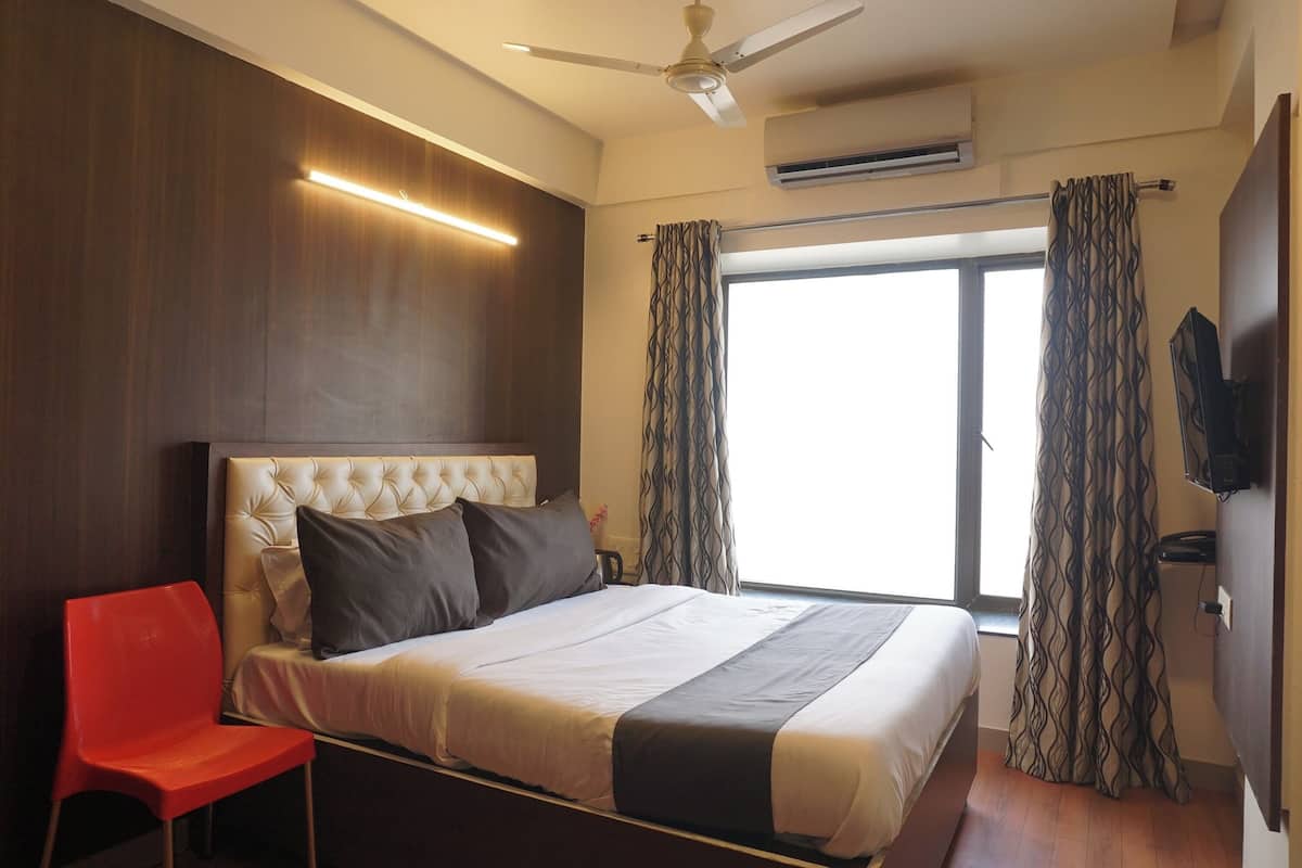 A hotel room with a bed, a red chair, a ceiling fan, and a window with curtains.