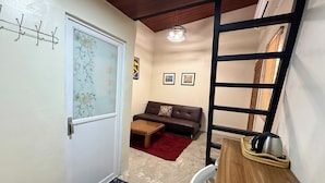 Un espacio habitable compacto con sofá, mesa de centro y una pequeña zona de cocina con hervidor.
