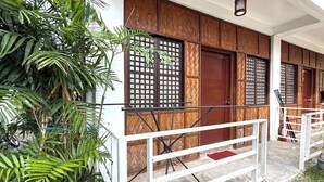 Un edificio tradicional con puertas y ventanas de madera, barandal de balcón blanco y una planta en maceta.