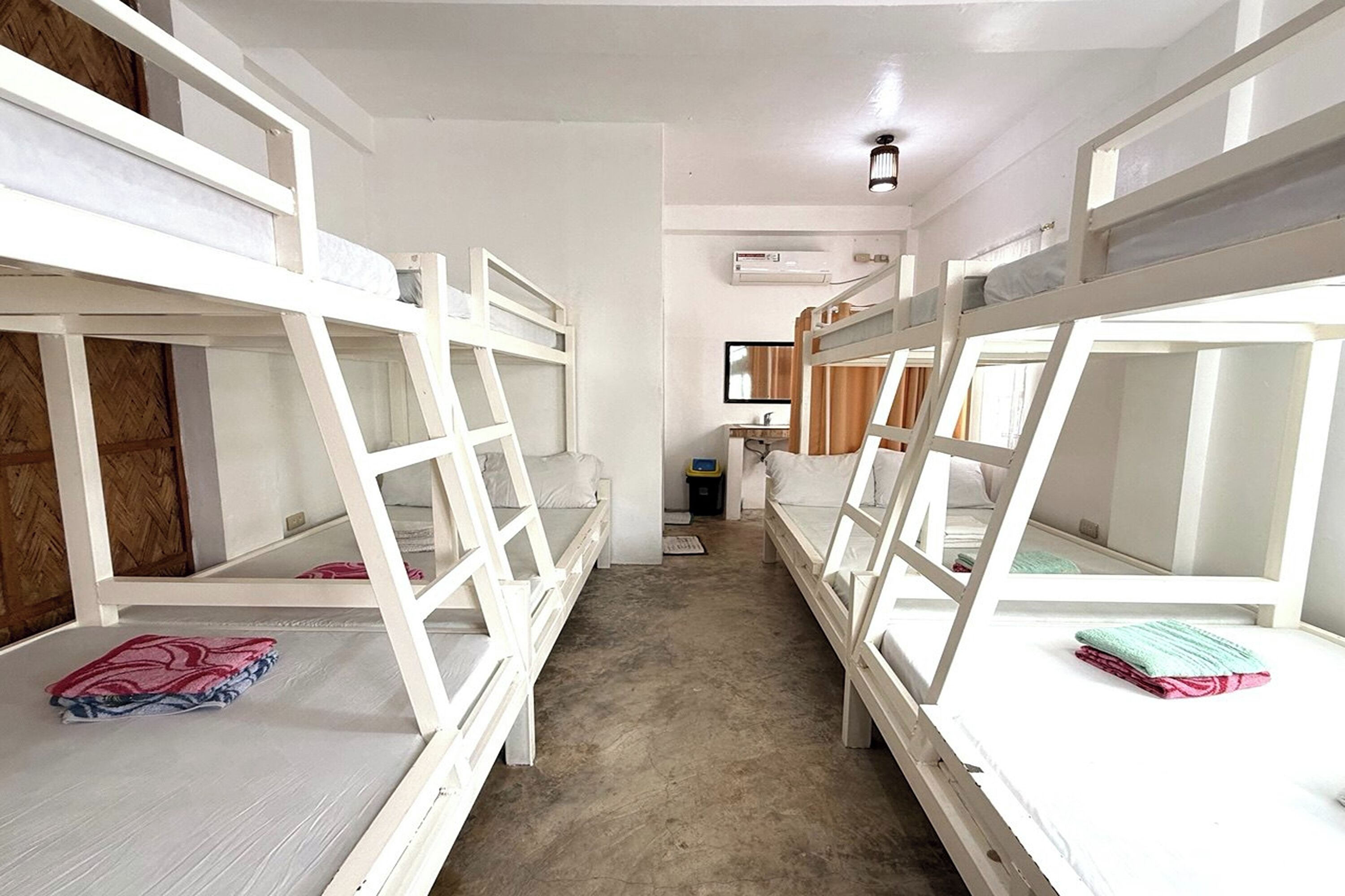 A dormitory room with bunk beds, a small desk, and a mirror.