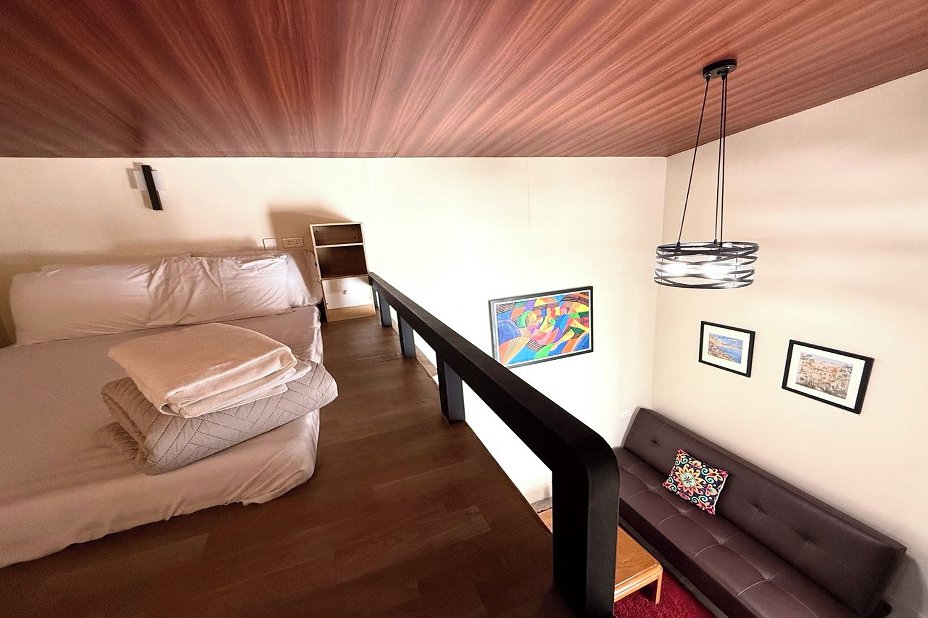 A bedroom with a bed, a sofa, a desk, and a hanging light fixture.