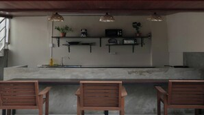 Una cocina con encimera de hormigón, sillas de madera y luces colgantes.