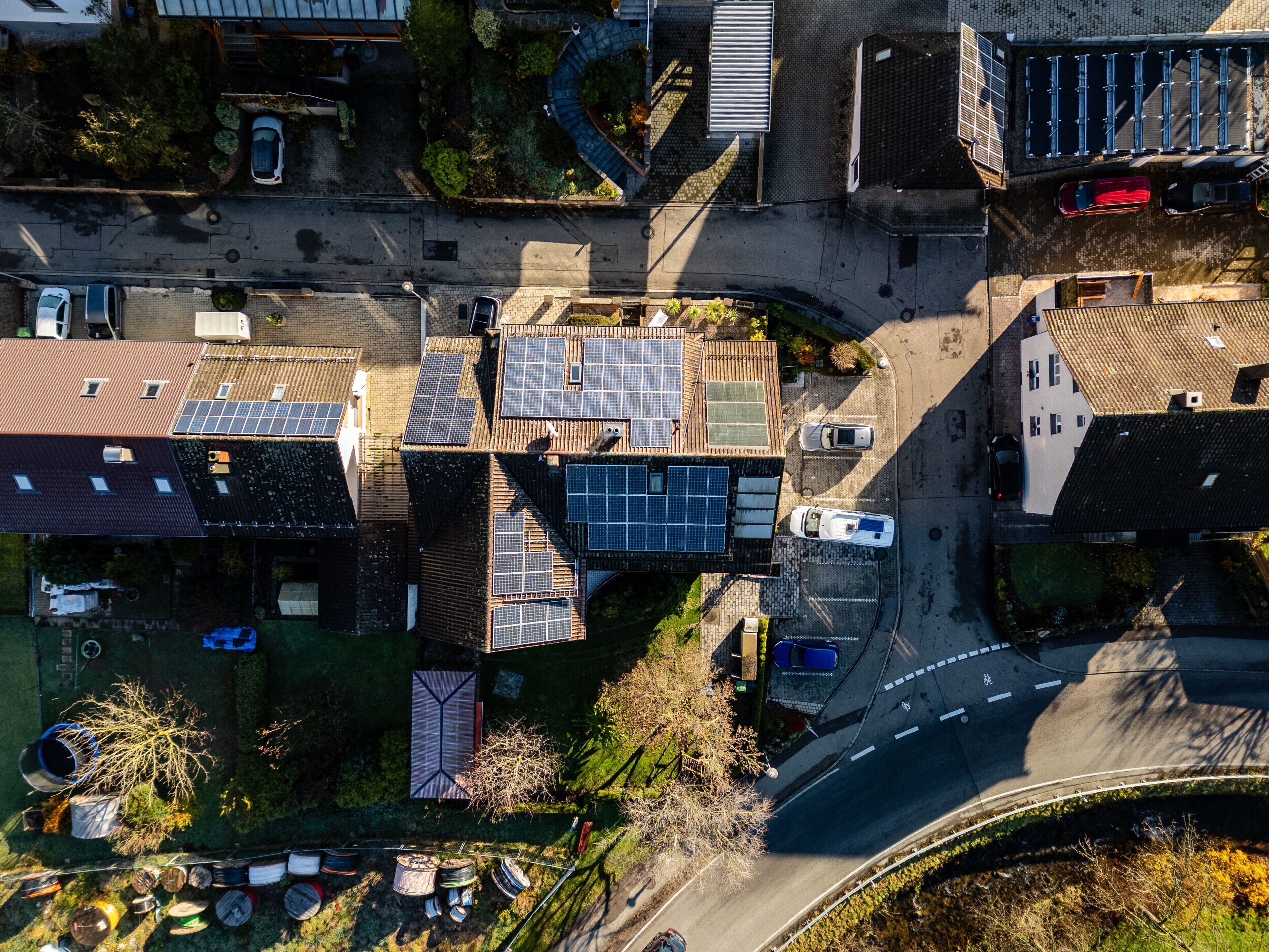 Eine Vogelperspektive eines Wohngebiets mit Solaranlagen auf den Dächern, einer gewundenen Straße und geparkten Autos.