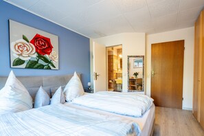 A bedroom with a bed, pillows, a painting of roses, a wooden door, and a bathroom visible through an open door. - Room 'Doppelzimmer Trimm Dich-stüble' with Shared Terrace, Shared Garden and Wi-Fi (Oberharmersbach)