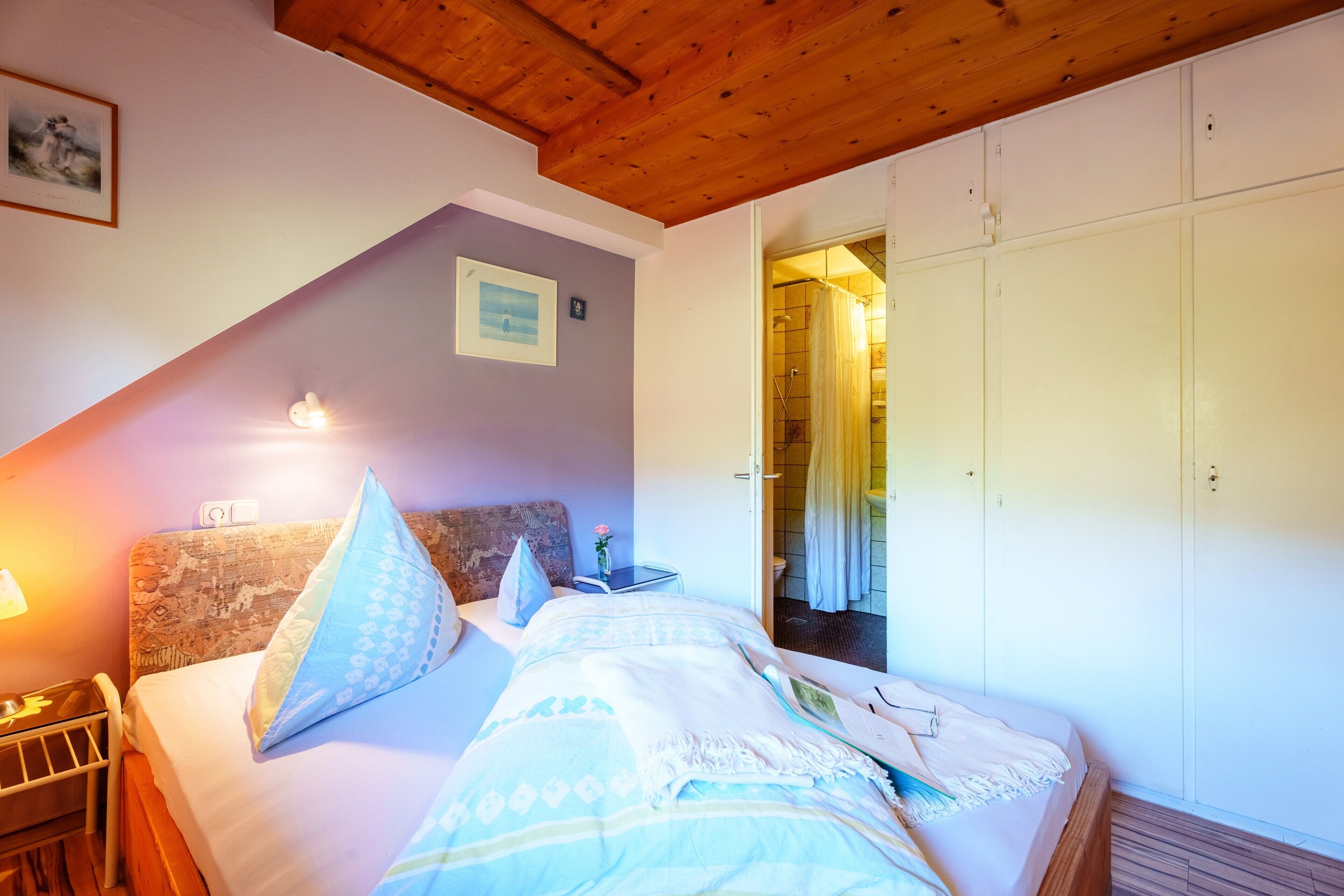 Een slaapkamer met een houten plafond, een bed met behang, een nachtkastje en een kledingkast.