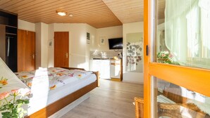 Een slaapkamer met een bed, houten plafond, kitchenette en een televisie aan de muur.