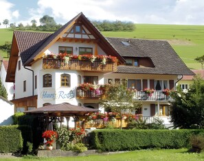 A two-story building with a balcony adorned with flowers, a sign reading 'Haus Rose,' and a garden area with potted plants. - Apartment 'Himmelreich' with Shared Terrace, Garden and Wi-Fi (Oberharmersbach)