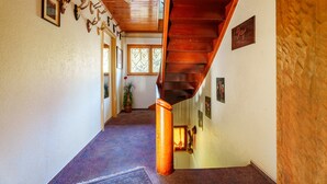 Un escalier en bois menant à un deuxième étage, un couloir orné de trophées de cervidés accrochés au mur, et une plante en pot près d’une fenêtre.