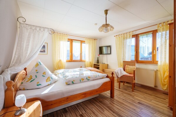 A bedroom with a wooden bed, a bedside table, a chair, a TV, and a window with curtains. - Apartment 'Himmelreich' with Shared Terrace, Garden and Wi-Fi (Oberharmersbach)