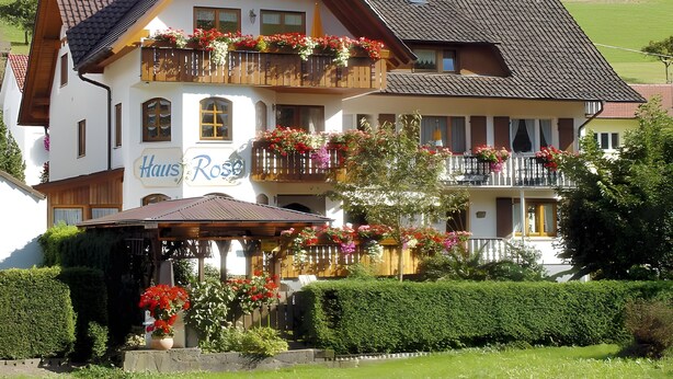 A two-story building with a balcony adorned with flowers, a sign reading 'Haus Rose,' and a garden area with potted plants. - Apartment 'Sonnenschein' with Shared Terrace, Garden and Wi-Fi (Oberharmersbach)