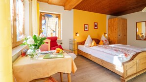 Een kamer met een houten plafond, een bed met wit beddengoed, een tafel met een bloevas en een stoel.