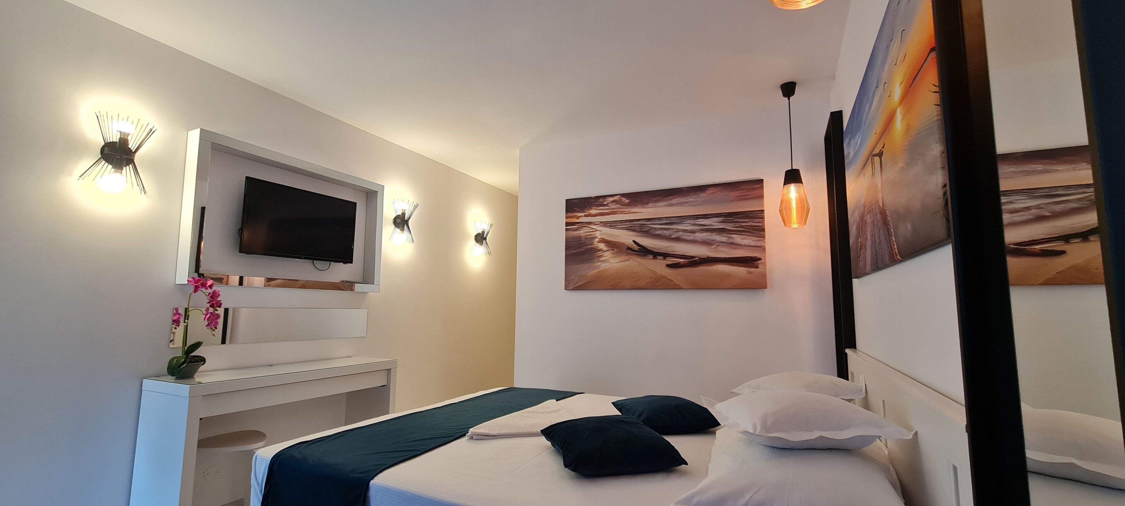 A bedroom with a bed, a TV, wall-mounted lights, and artwork.