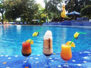 Un área junto a la piscina con tres bebidas sobre una mesa de baldosas.