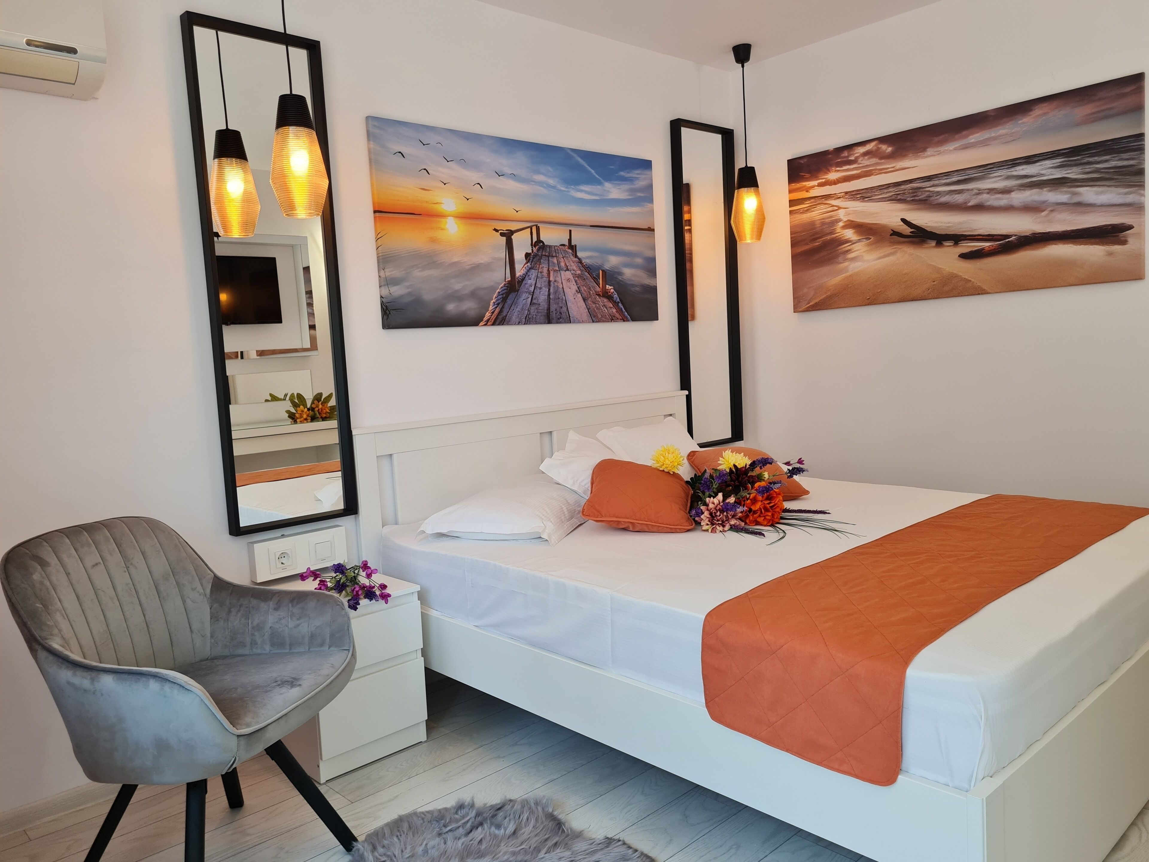 Un dormitorio con cama, una silla, una mesita de noche, un espejo y dos lámparas de pared.