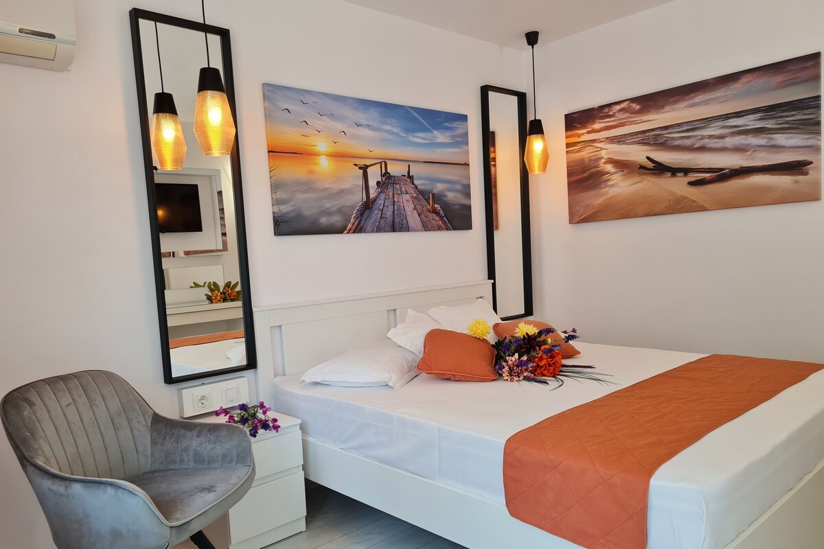 A bedroom with a bed, a chair, a nightstand, a mirror, and two wall-mounted lamps.