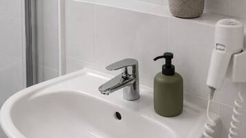 A bathroom sink with a chrome faucet, a green soap dispenser, and a white hairdryer on a wall-mounted shelf.