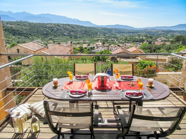 A dining table set outdoors with a scenic view of a village and mountains in the background.