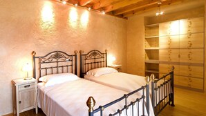 A bedroom with two beds, wooden ceiling beams, a nightstand with a lamp, and a wardrobe with a mirror.
