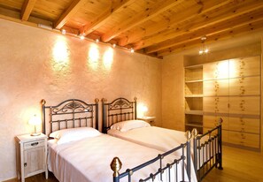 A bedroom with two beds, wooden ceiling beams, a nightstand with a lamp, and a wardrobe with a mirror.