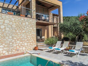 A poolside area with lounge chairs and a stone wall. - Apokoron Villa Aphrodite with Private Pool (Gavalochori)