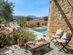 A poolside area with a stone wall, lounge chairs, a table with wine glasses, and a view of a mountain.