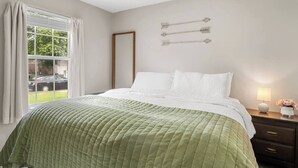 Une chambre à coucher avec un lit, une table de chevet, une lampe et une fenêtre avec des rideaux.