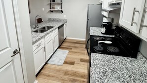 A kitchen with white cabinets, a granite countertop, a black stove, and a wooden floor. - 3 KING BEDS Furr-Friendly Fayetteville Retreat (Fayetteville)