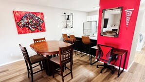 A modern kitchen with white cabinets, a red accent wall, and a wooden dining table with chairs. - 3 KING BEDS Furr-Friendly Fayetteville Retreat (Fayetteville)