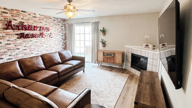 A modern living room with a brick wall, leather sofa, wooden coffee table, and a flat-screen TV. - 3 KING BEDS Furr-Friendly Fayetteville Retreat (Fayetteville)