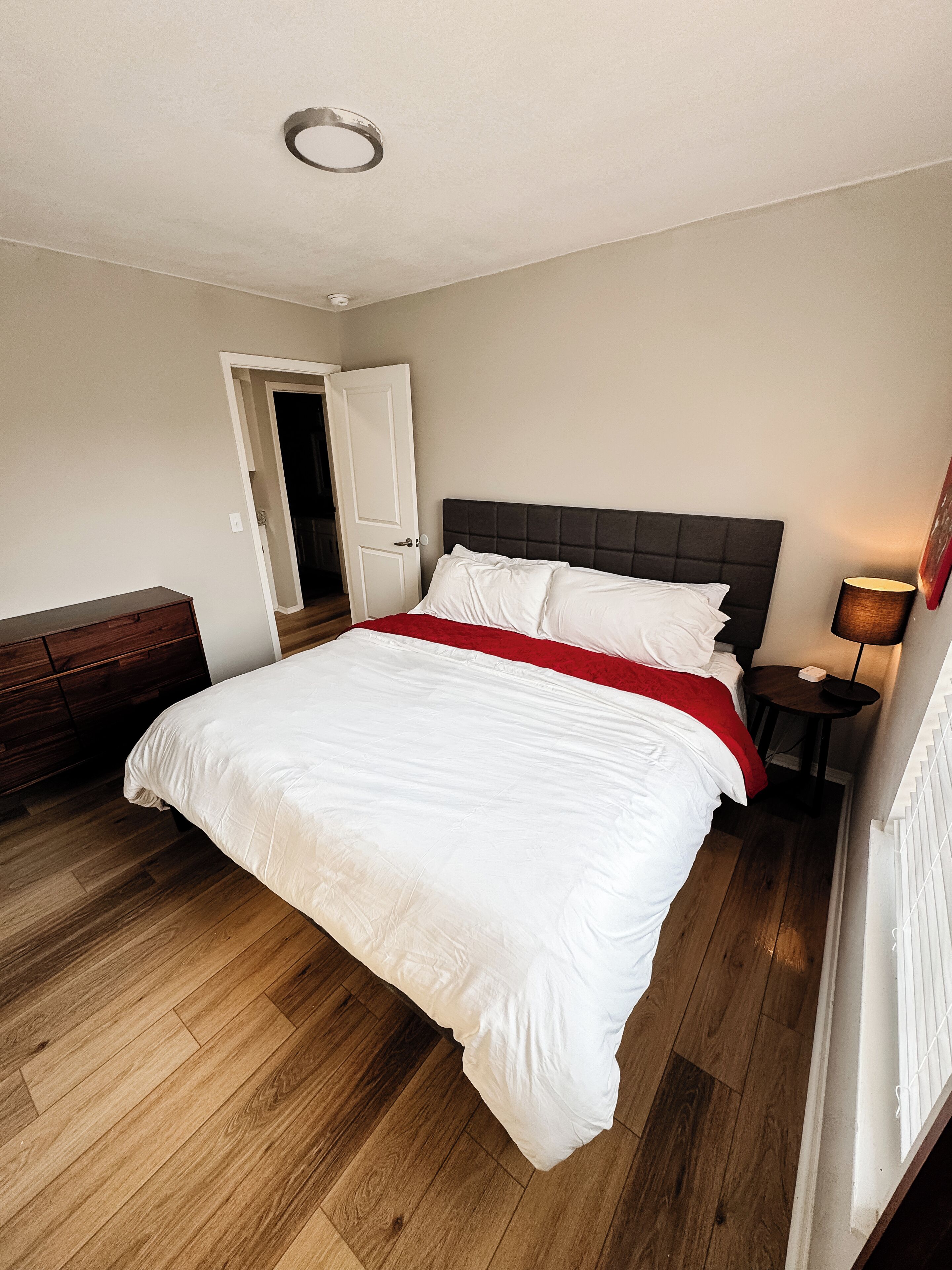Ein Schlafzimmer mit einem großen Bett, einem Nachttisch, einer Lampe und einer Tür zu einem anderen Raum.
