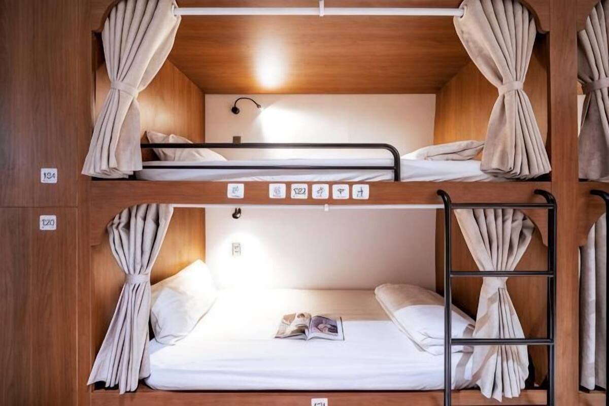 Quarto com beliches, cortinas, escada e uma pequena mesa com uma revista.