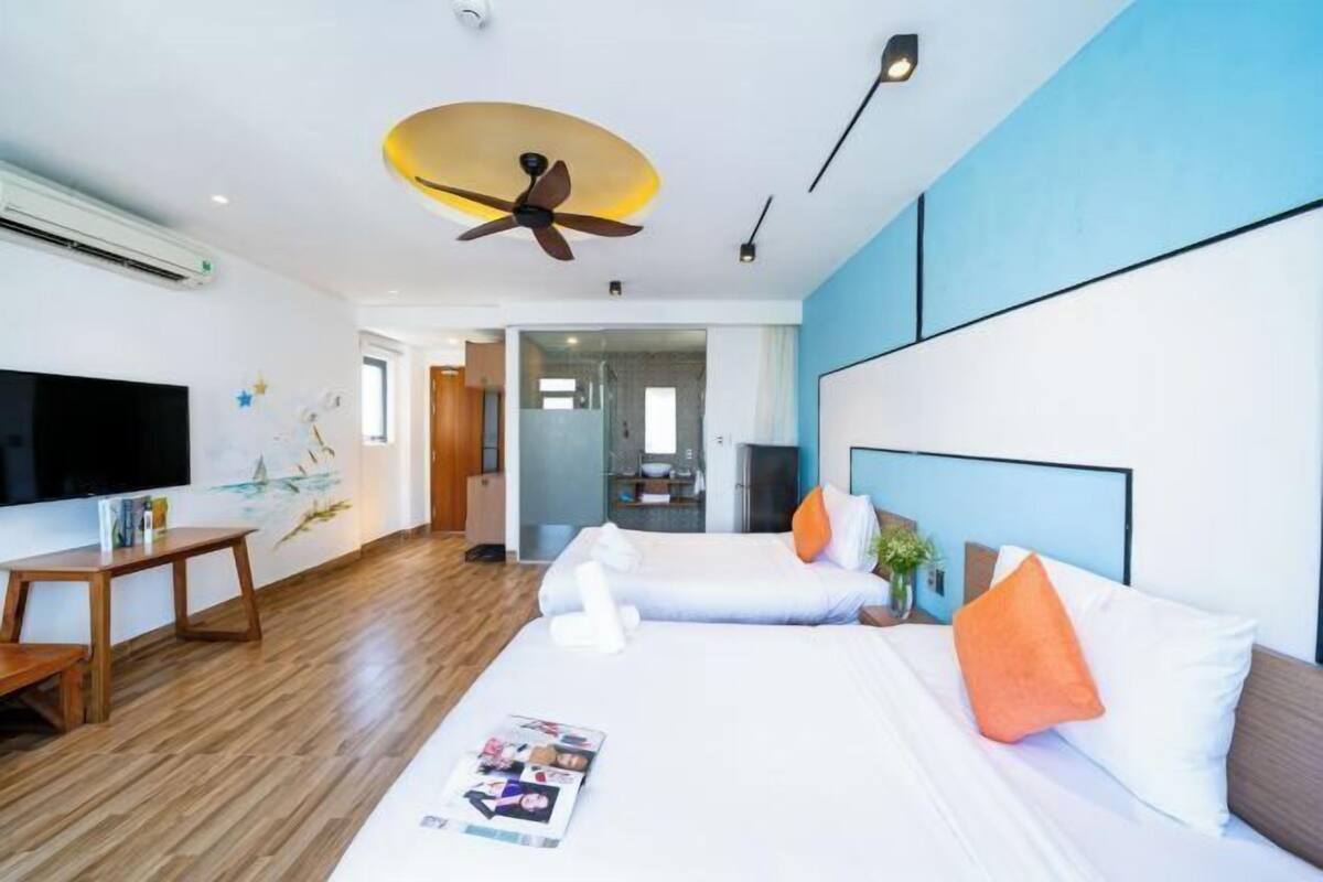 Quarto de hotel com cama, escrivaninha, televisão e ventoinha no teto.