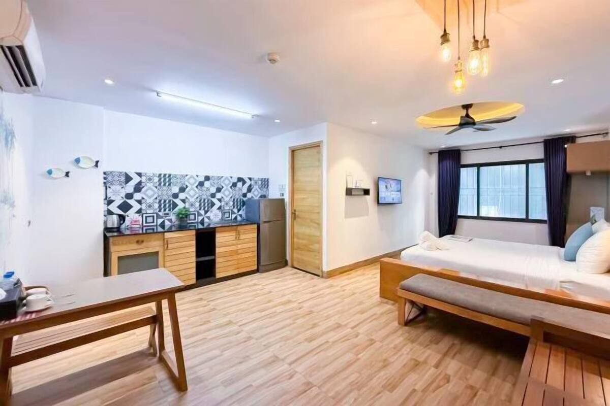 Quarto de hotel moderno com cama, uma secretária pequena, uma kitchenette e um ventilador de teto.