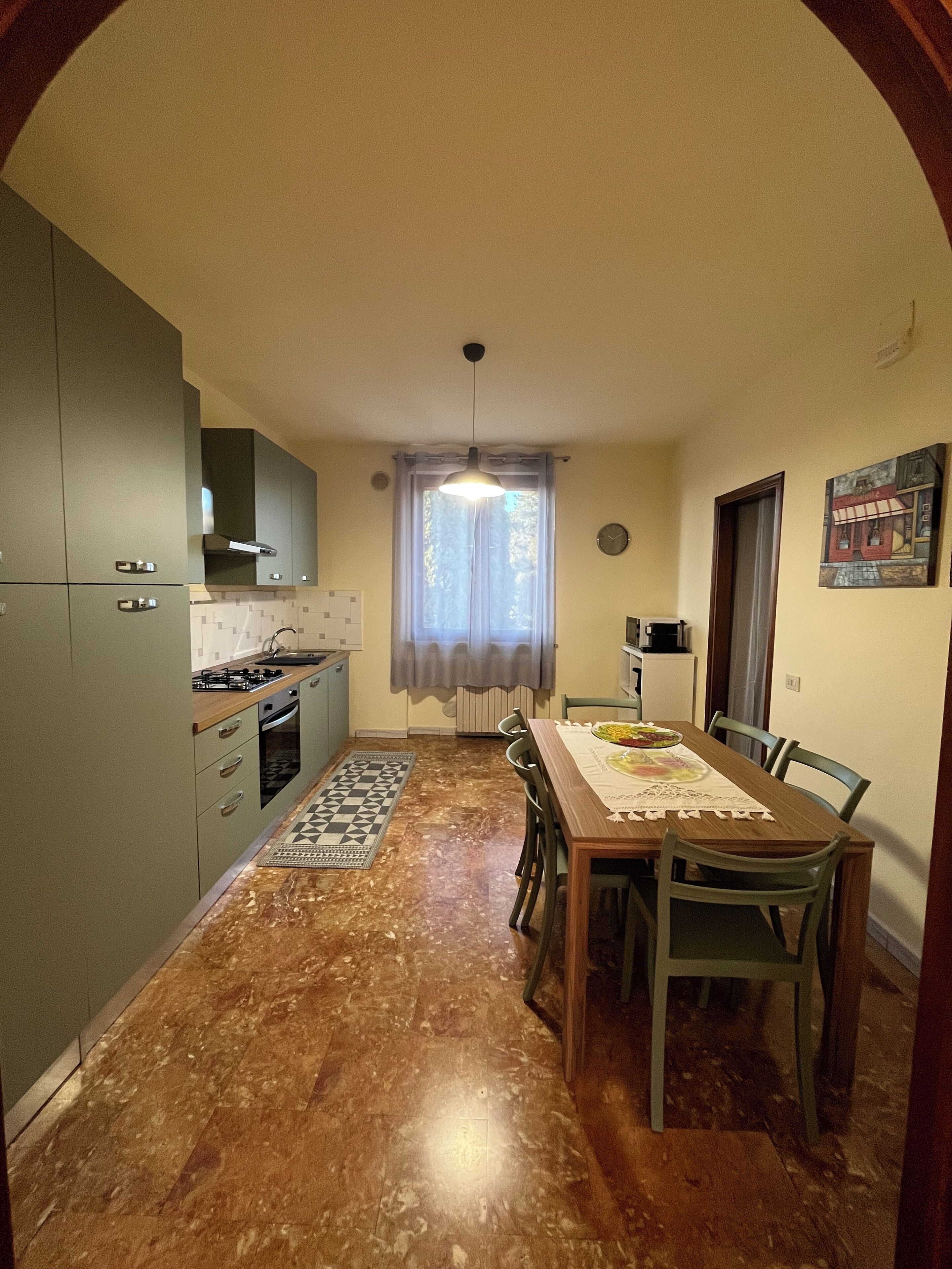 Uma cozinha compacta com uma mesa de jantar e cadeiras, uma janela com cortinas e um relógio na parede.