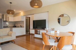 A modern living room with a sofa, dining table, chairs, a TV, and a kitchen area with a stove and cabinets.