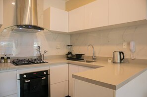 A modern kitchen with a stainless steel range hood, a built-in oven, a coffee maker, and a kettle.