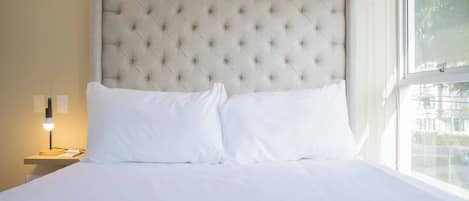 A neatly made bed with a tufted headboard, white bedding, and a bedside lamp.