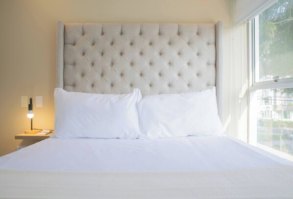 A neatly made bed with a tufted headboard, white bedding, and a bedside lamp.