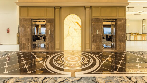 A lobby with a marble floor, a large central archway, and mirrored walls reflecting the interior.