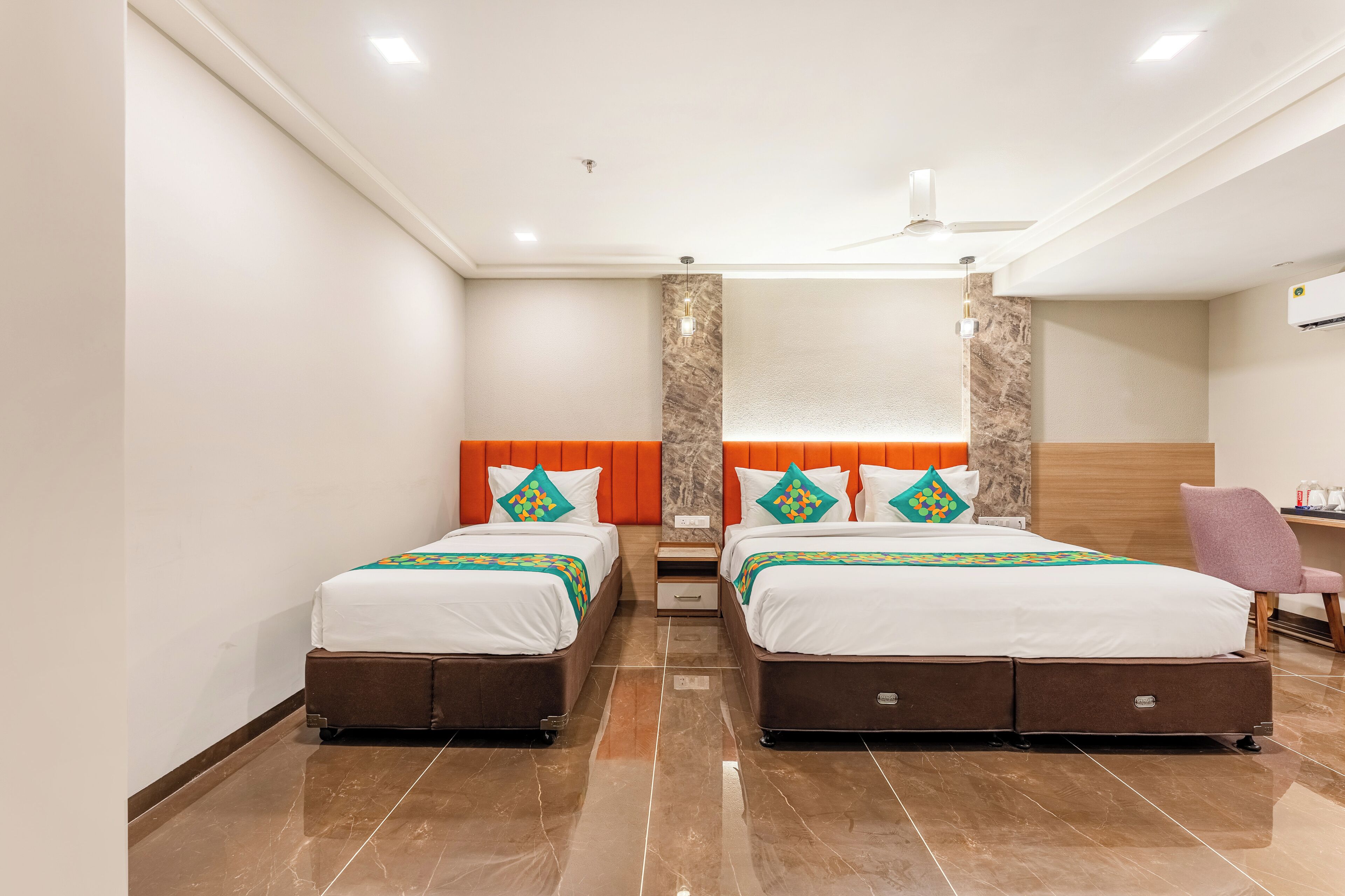 A hotel room with two beds, a marble accent wall, a ceiling fan, and a small desk with a chair.