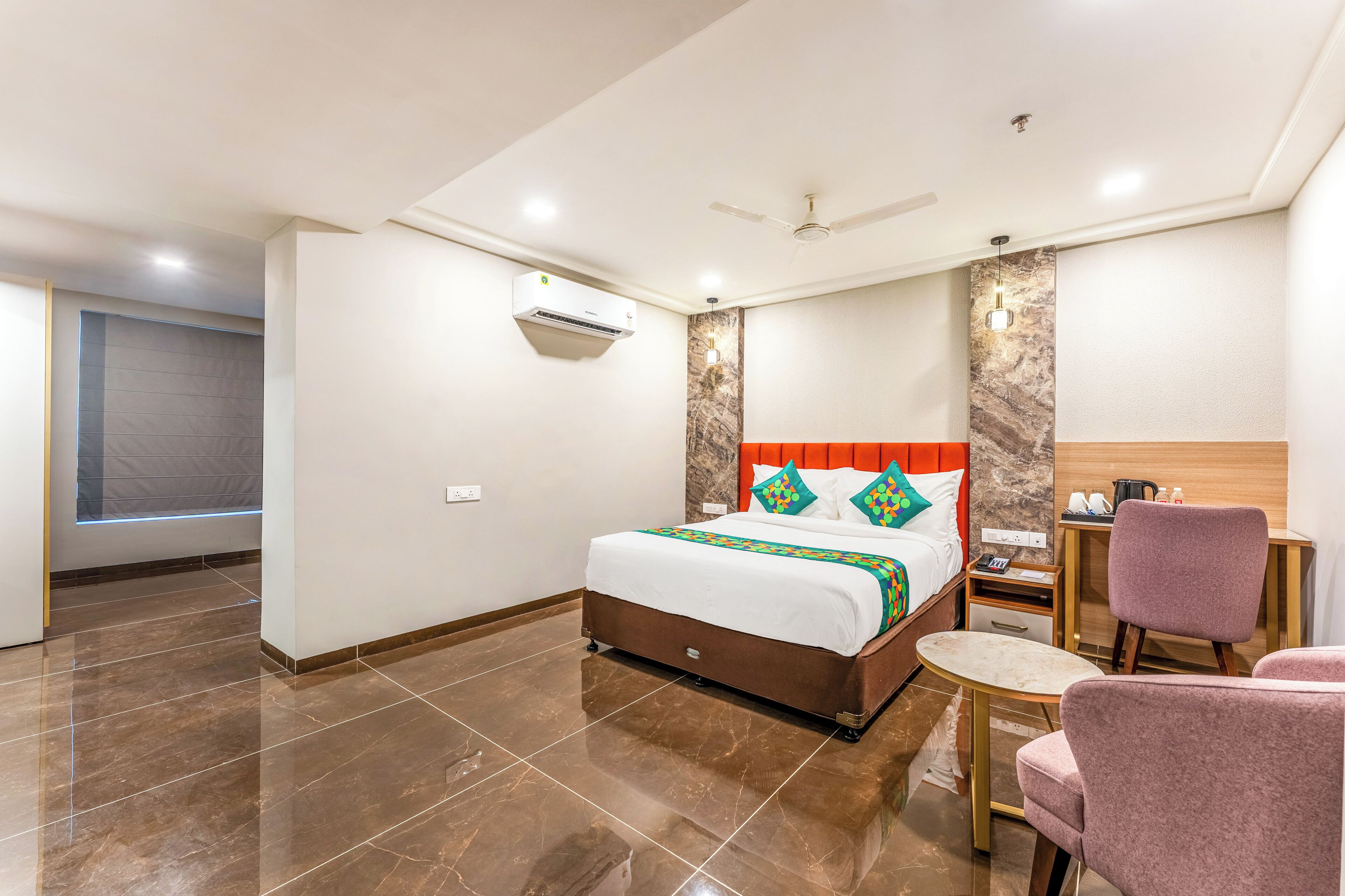 A modern hotel room with a large bed, a desk, a chair, and a small table.