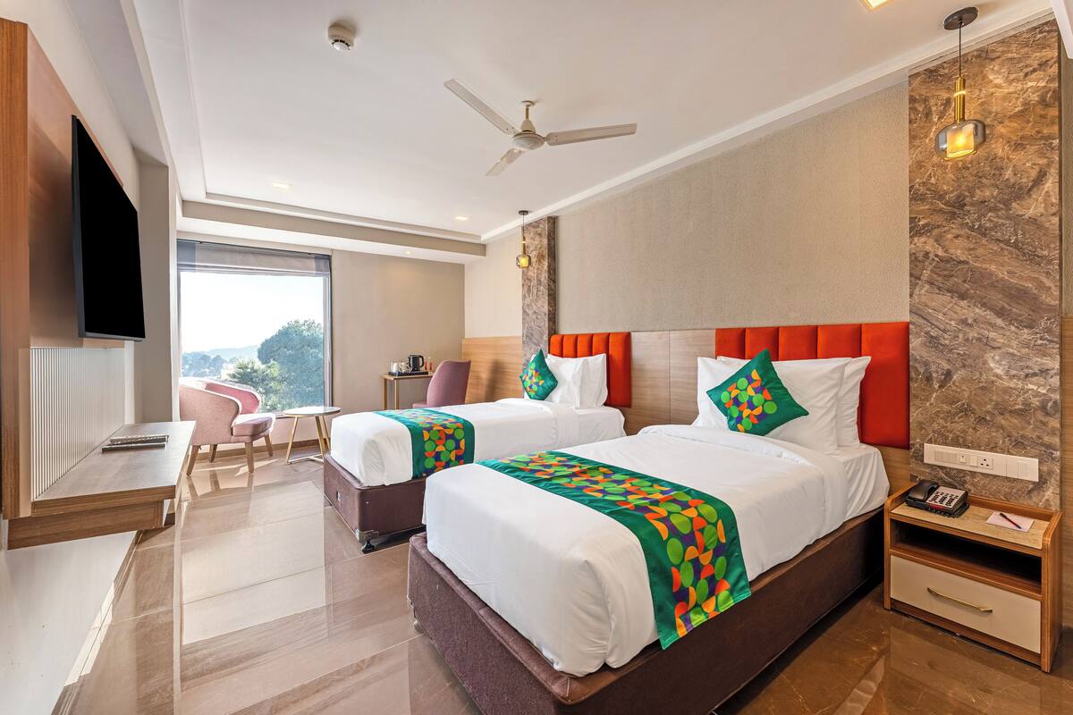 A hotel room with two beds, a desk, a chair, a TV, and a view of the outdoors.
