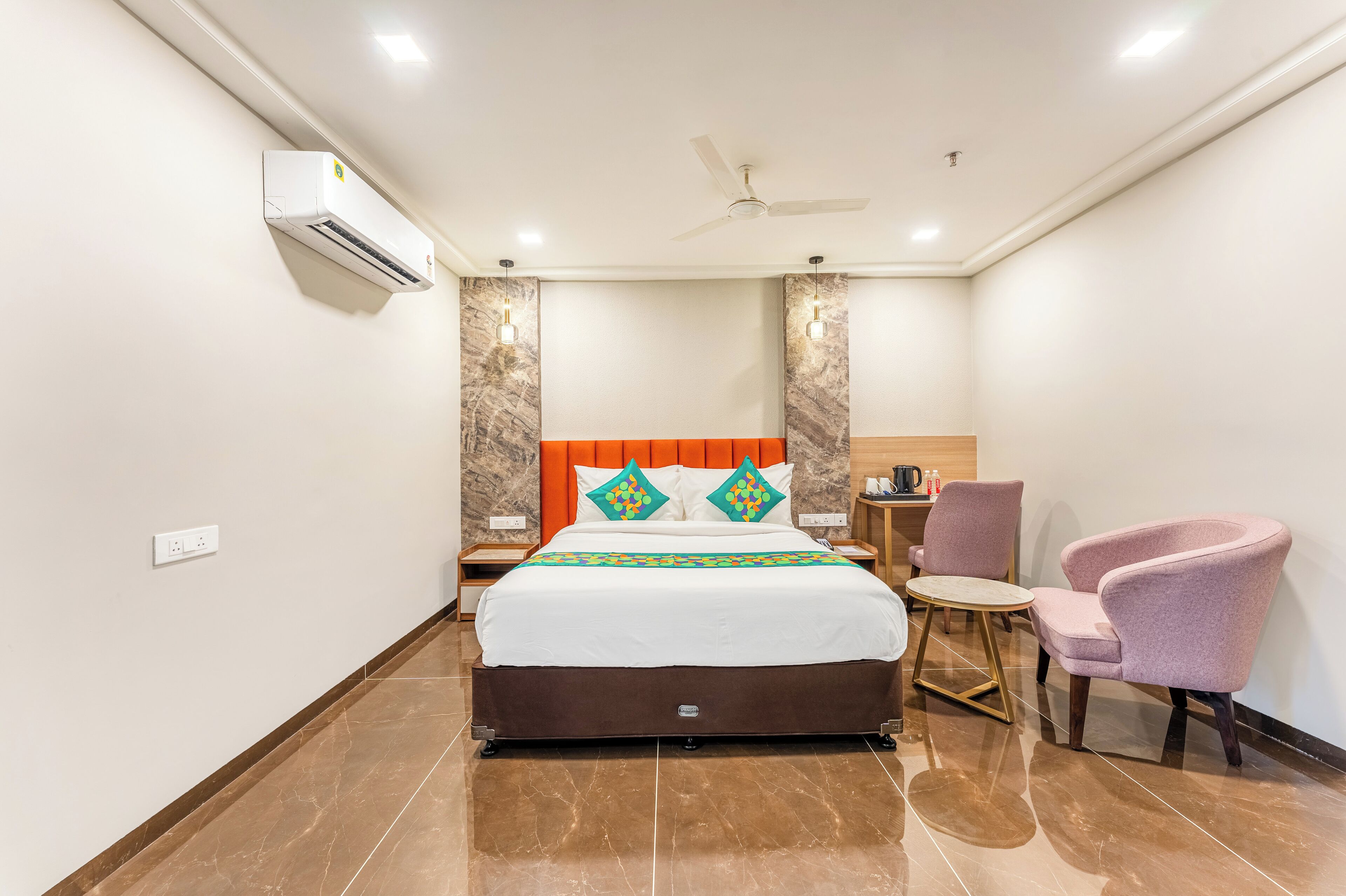 A hotel room with a bed, a ceiling fan, an air conditioner, a nightstand, a chair, and a small table.